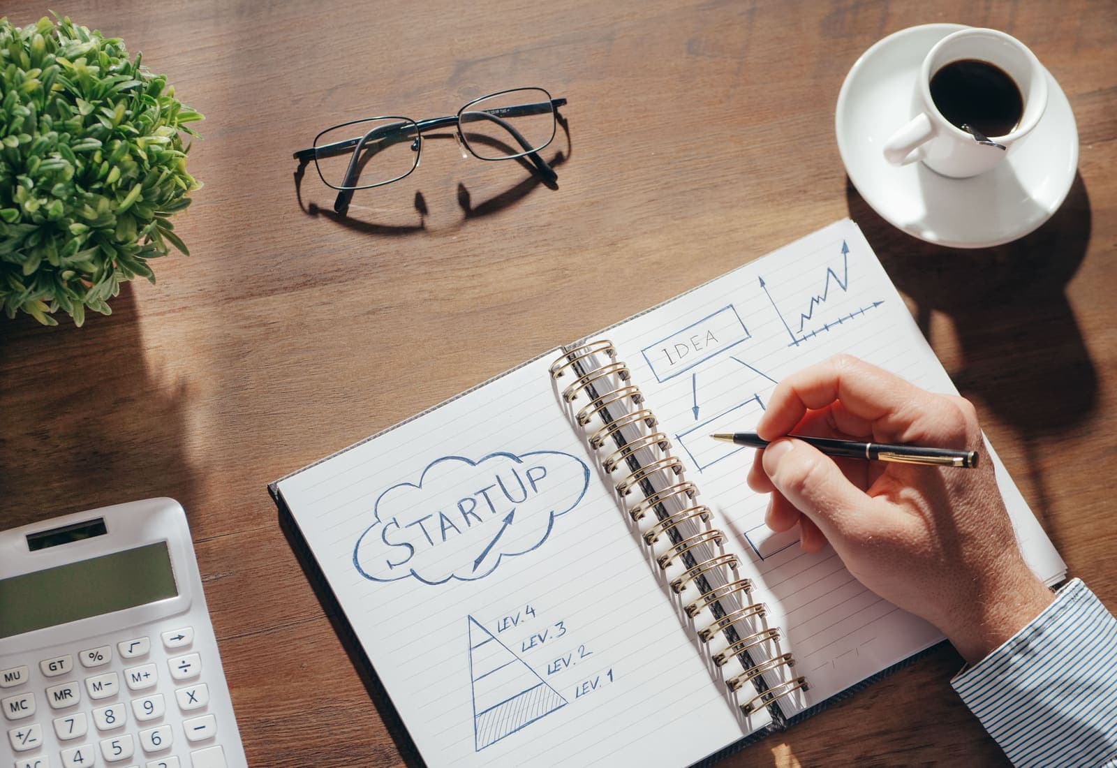 Entrepreneur writing a startup plan in a notebook with a calculator and coffee